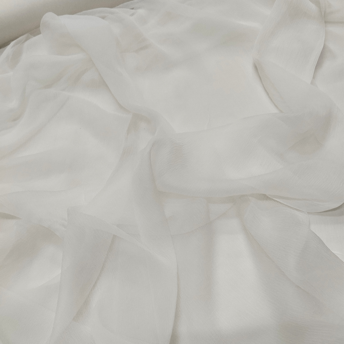 Soft white 30×30 dyeable chiffon fabric with transparent lightweight texture and elegant flowing drape held in hand.